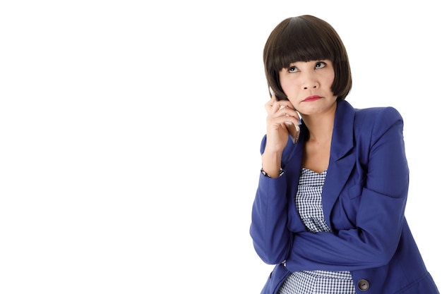 Joven mujer asiática en elegante traje azul con desagradable llamada telefónica y mirando pensativamente aislado sobre fondo blanco.