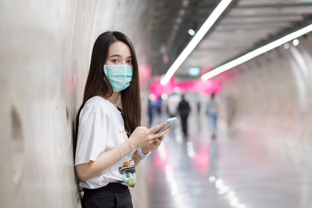 Joven mujer asiática se encuentra en el túnel del metro y usa una mascarilla como nueva normalidad y atención médica