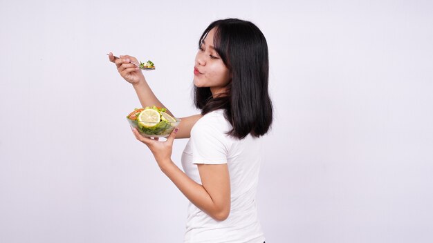 Joven mujer asiática feliz comiendo ensalada saludable con superficie blanca aislada