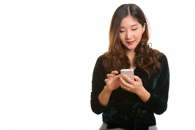 Joven mujer asiática feliz mediante teléfono móvil aislado contra un blanco