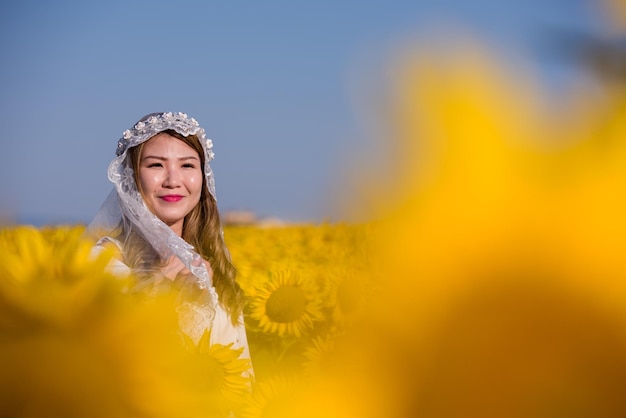 Joven mujer asiática feliz con vestido de novia divirtiéndose y relajándose en el campo de girasol