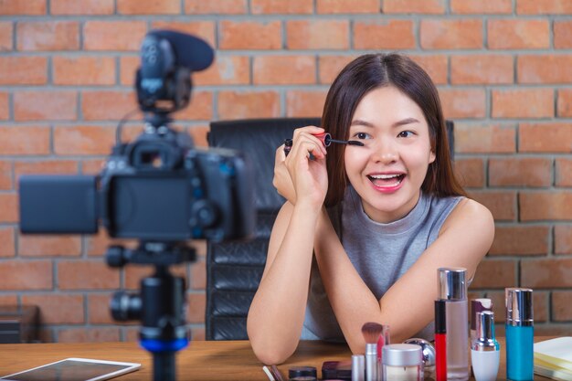 Joven mujer asiática feliz vlogging a su página de fans que muestra cómo poner maquillaje en