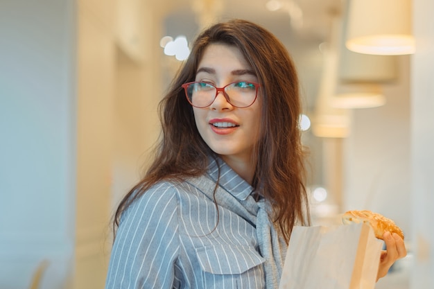 Joven mujer asiática con gafas rojas con pasteles con bolsa de papel en la panadería