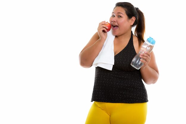 Joven mujer asiática gorda feliz sonriendo mientras sostiene una manzana roja y una botella de agua