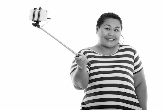 Joven mujer asiática gorda feliz sonriendo mientras toma selfie foto con teléfono móvil en selfie stick