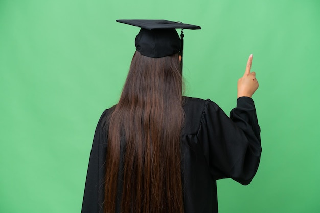 Joven mujer asiática graduada universitaria sobre antecedentes aislados apuntando hacia atrás con el dedo índice