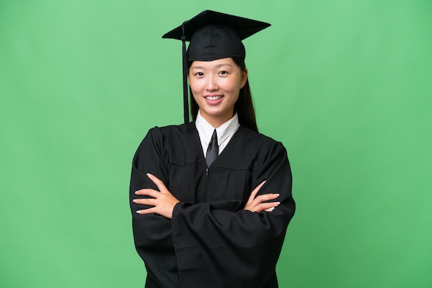 Joven mujer asiática graduada universitaria sobre un fondo aislado manteniendo los brazos cruzados en posición frontal