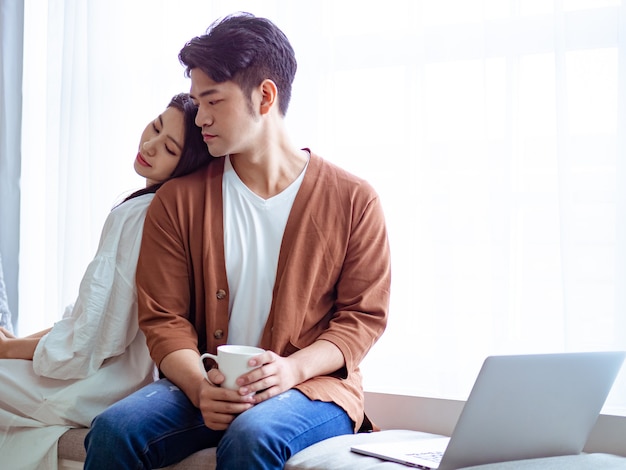 Joven mujer asiática y hombre en casa con una taza de café en las manos.