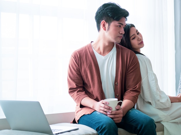 Joven mujer asiática y hombre en casa con una taza de café en las manos.