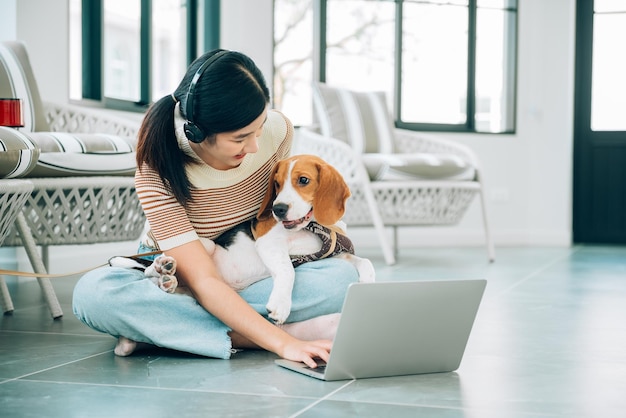 Joven mujer asiática independiente que trabaja en línea a través de las redes sociales con un perro Beagle usando una computadora portátil en la sala de estar de su casa