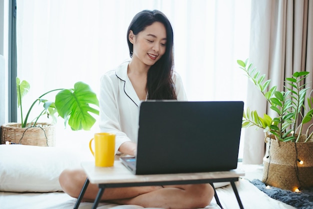 Joven mujer asiática independiente que trabaja en el trabajo de negocios en una computadora portátil en casa trabajando desde el concepto de hogar