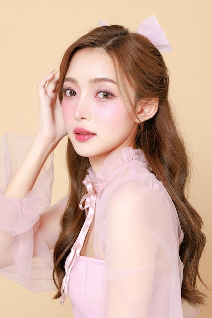 Joven mujer asiática linda en un vestido rosa elegante maquillaje de estilo coreano hidratado suave piel perfecta en un fondo beige tratamiento facial cosmetología cirugía plástica