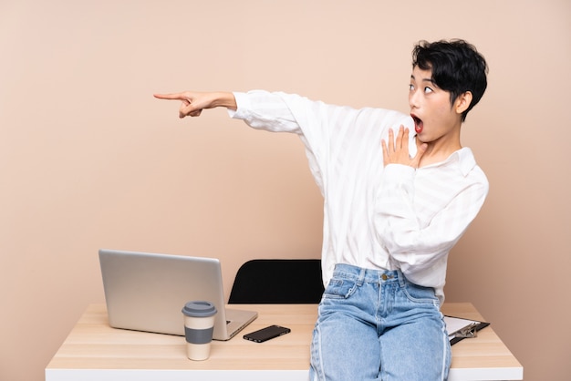 Joven mujer asiática de negocios en su lugar de trabajo apuntando con el dedo al lado