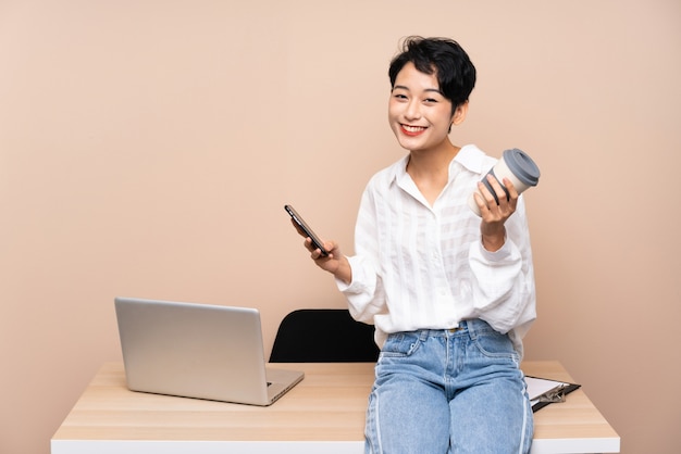 Joven mujer asiática de negocios en su lugar de trabajo con café para tak