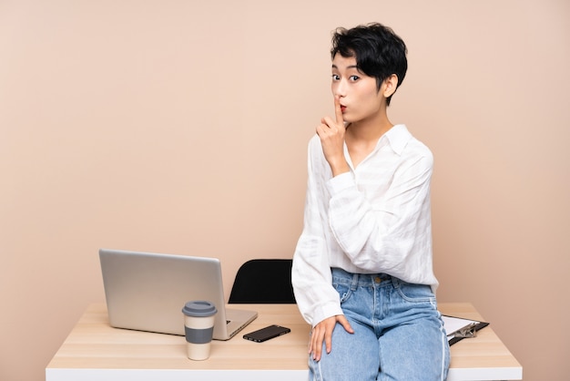 Joven mujer asiática de negocios en su lugar de trabajo haciendo gesto de silencio