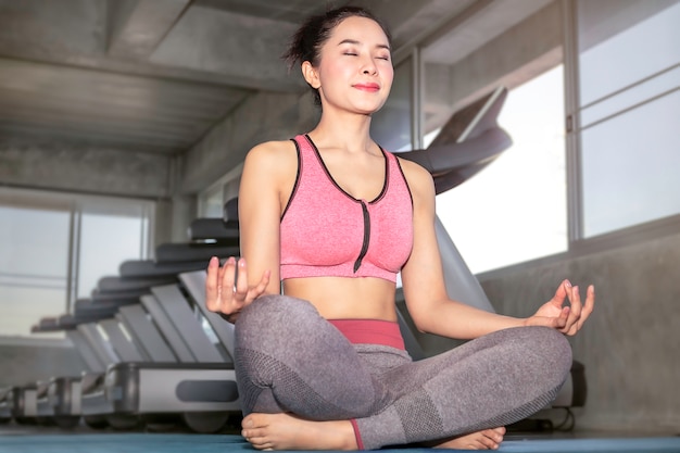 Joven mujer asiática practicando yoga en el gimnasio. Pose de loto en la sesión de meditación.