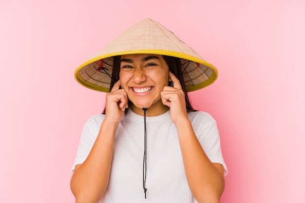 Joven mujer asiática que llevaba un sombrero vietnamita aislado Joven mujer asiática que llevaba un sombrero vietnamina para cubrir las orejas con las manos.