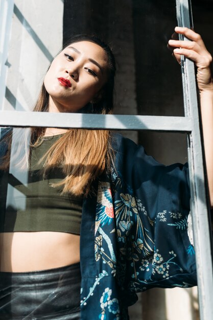 Joven mujer asiática en ropa casual moderna mirando por la ventana