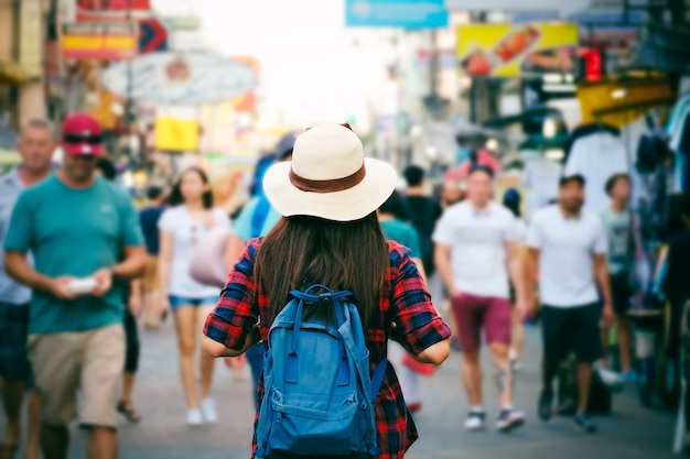 Joven mujer asiática con sombrero y mochila viajando en mercado entre personas