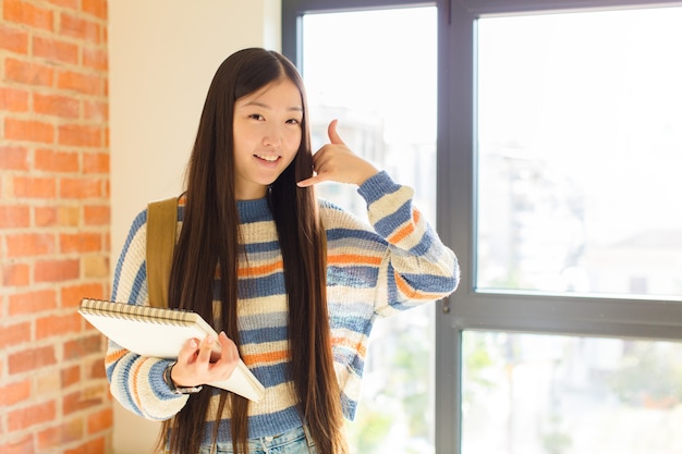 Joven mujer asiática sonriendo y haciendo un gesto de llamada