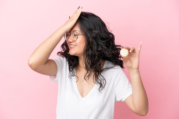 Foto joven mujer asiática sosteniendo un bitcoin aislado sobre fondo rosa se ha dado cuenta de algo y tiene la intención de la solución