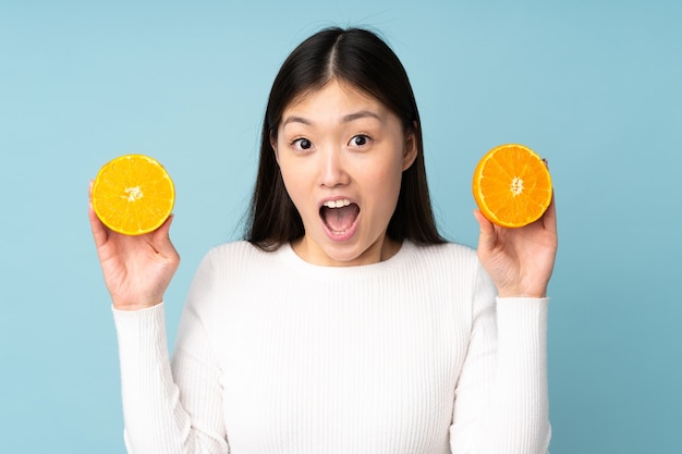 Joven mujer asiática sosteniendo una naranja sobre fondo azul aislado