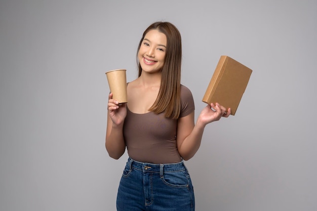 Joven mujer asiática sosteniendo un vaso de papel y una caja de papel sobre fondo blanco Concepto de salvar la tierra