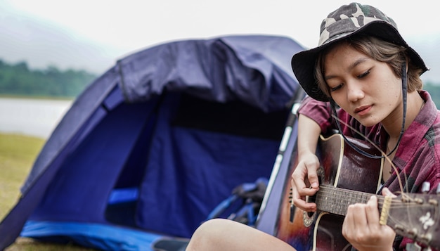 Joven mujer asiática tocando la guitarra en el camping