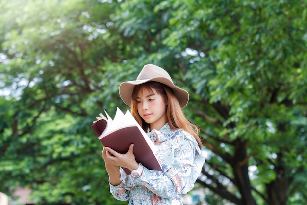 Joven mujer asiática en vestido retro abriendo un libro en el parque