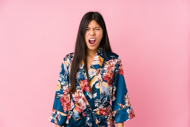 Joven mujer asiática vistiendo un kimono pijama gritando muy enojado y agresivo.
