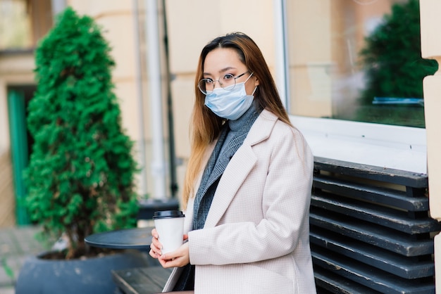 Joven mujer asiática vistiendo mascarilla de pie en una calle doméstica