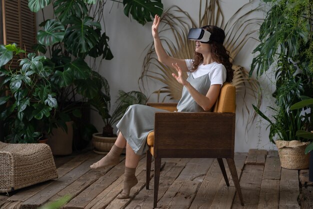 Foto joven mujer asombrada con auriculares de realidad virtual descansando en un invernadero cubierto lleno de plantas tropicales y exóticas