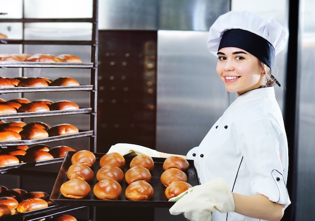 Una joven mujer atractiva Baker en una chaqueta y gorra de chef blanca