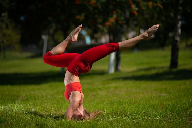 Joven mujer atractiva practicando yoga al aire libre, la niña realiza una parada de manos boca abajo