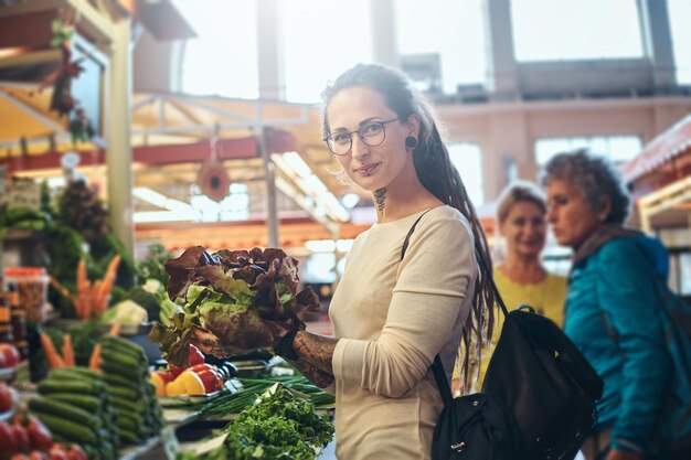 Joven mujer atractiva con tatuajes eligiendo ensalada fresca en el mercado de verduras.