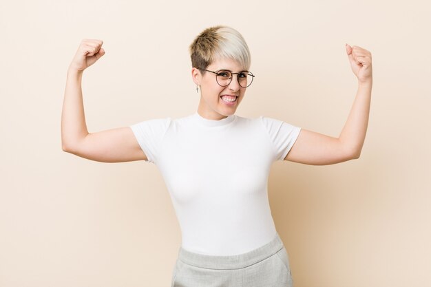 Joven mujer auténtica y natural con una camisa blanca que muestra un gesto de fuerza con los brazos, símbolo del poder femenino