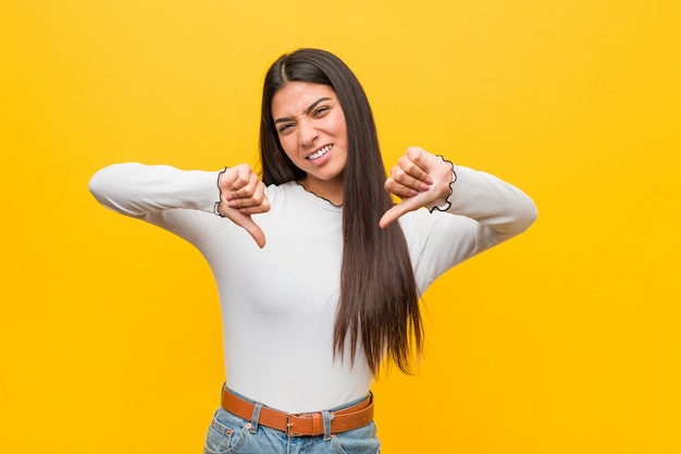 Foto joven mujer bastante árabe contra un amarillo mostrando el pulgar hacia abajo y expresando aversión.