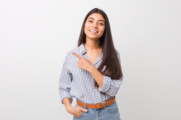 Joven mujer bastante árabe sonriendo y señalando a un lado, mostrando algo en el espacio en blanco.