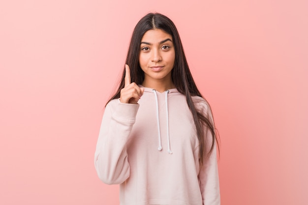 Joven mujer bastante árabe vistiendo un deporte casual look mostrando número uno con el dedo.