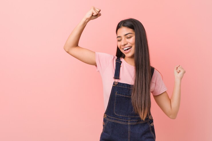Foto joven mujer bastante árabe vistiendo un mono de jeans levantando el puño después de una victoria, concepto ganador.