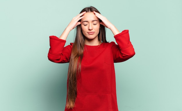 Joven mujer bastante casual que parece concentrada, pensativa e inspirada, intercambiando ideas e imaginando con las manos en la frente