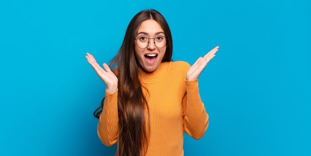 Joven mujer bastante casual que parece feliz y emocionada, sorprendida con una sorpresa inesperada con ambas manos abiertas junto a la cara