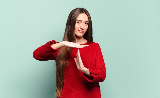 Joven mujer bastante casual que parece seria, severa, enojada y disgustada, haciendo el signo de tiempo de espera