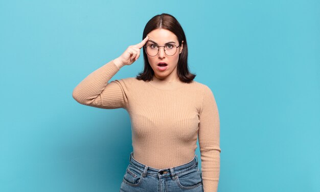 Joven mujer bastante casual que parece sorprendida, con la boca abierta, conmocionada, dándose cuenta de un nuevo pensamiento, idea o concepto