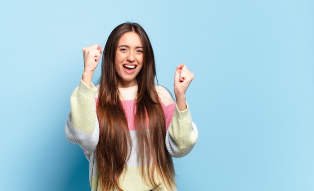 Joven mujer bastante casual que se siente feliz, positiva y exitosa, celebrando la victoria, los logros o la buena suerte