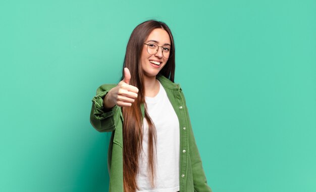 Joven mujer bastante casual que se siente orgullosa, despreocupada, segura y feliz, sonriendo positivamente con los pulgares hacia arriba