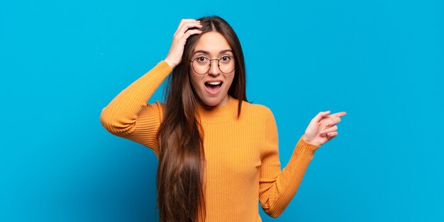 Joven mujer bastante casual riendo, luciendo feliz, positiva y sorprendida, dándose cuenta de una gran idea apuntando al espacio de copia lateral