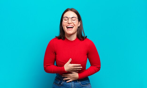 Joven mujer bastante casual riéndose a carcajadas de una broma hilarante, sintiéndose feliz y alegre