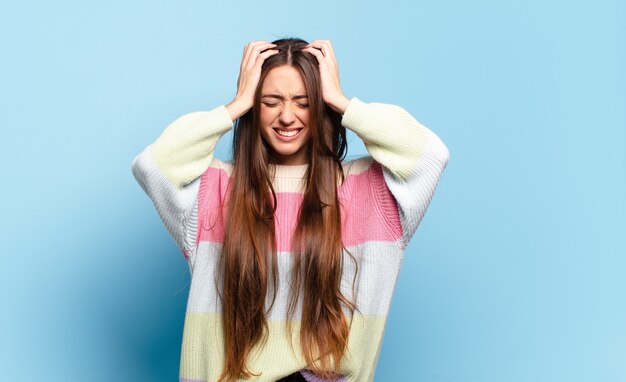 Joven mujer bastante casual sintiéndose estresada y frustrada, levantando las manos a la cabeza