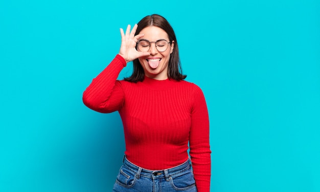 Joven mujer bastante casual sonriendo felizmente con cara divertida, bromeando y mirando por la mirilla, espiando secretos